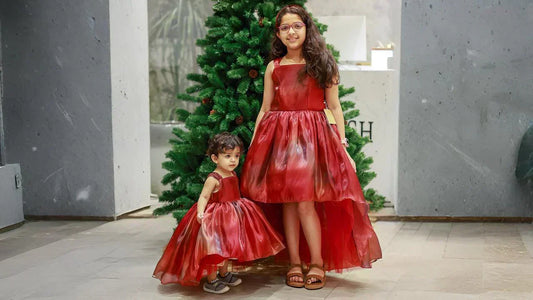 Two young girls wearing matching royal red multishade laser organza high-low party dresses in front of a Christmas tree.