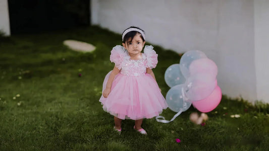 Beautiful baby girl wearing a trendy pink party wear dress and headband for a first birthday celebration photoshoot.