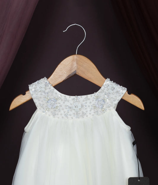 Close view of a off-white dress with beaded neckline on a wooden hanger against a dark background.