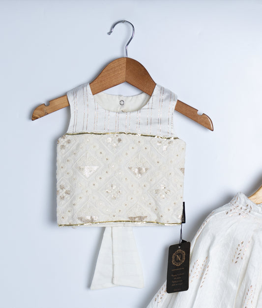 Traditional white kids’ ethnic outfit featuring a sleeveless embroidered blouse with delicate embellishments and a matching skirt with a soft yellow hem, displayed on wooden hangers against a light background.