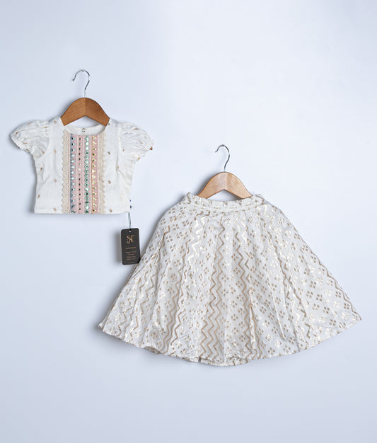 Two pieces of traditional Indian clothing, a top with vertical mirror work and lace edges, and a full-length skirt with a flowing flared design, both in off-white color, displayed on hangers against a white background.