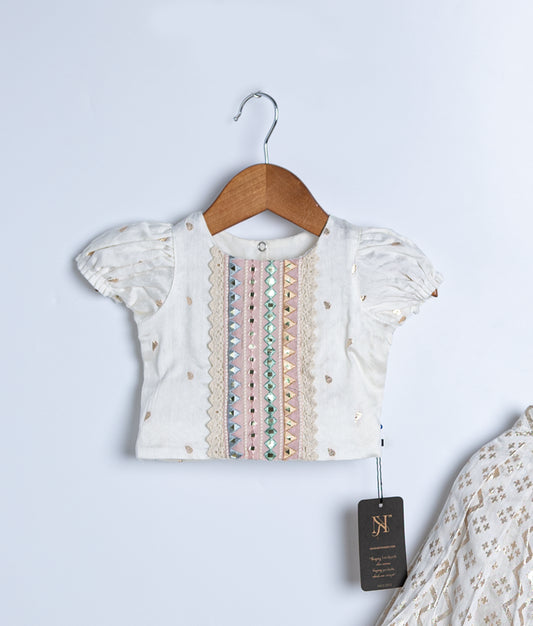Close View of a white ethnic blouse with puff sleeves, featuring pastel embroidery, mirror work, and gold accents—displayed on a wooden hanger for traditional or festive wear.