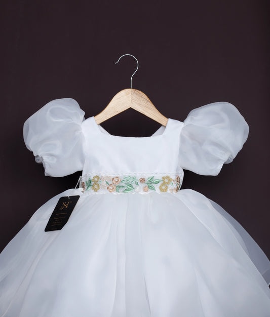 Close view of an off-white baby girl dress with puff sleeves and floral waistband—perfect for birthdays and special occasions