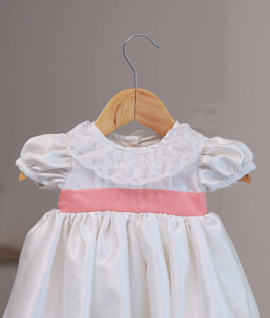 Close-up of intricate hand-embroidery and soft fabric detailing on an off-white baby girl christening ceremony dress