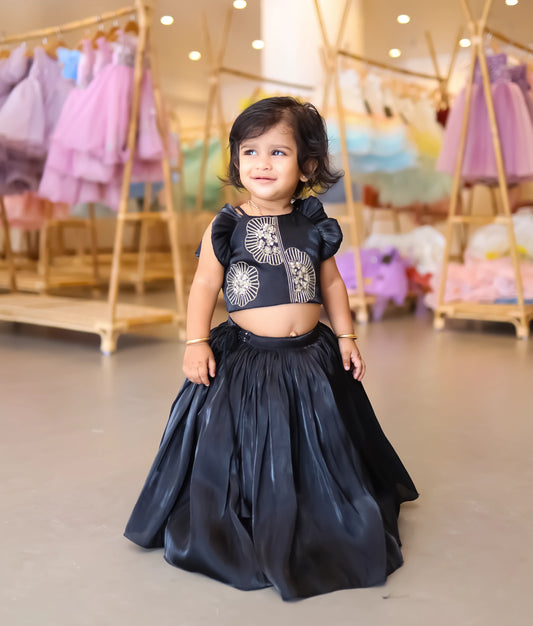 A baby girl wearing the black lacer organza skirt and top featuring golden floral embroidery and shoulder frills
