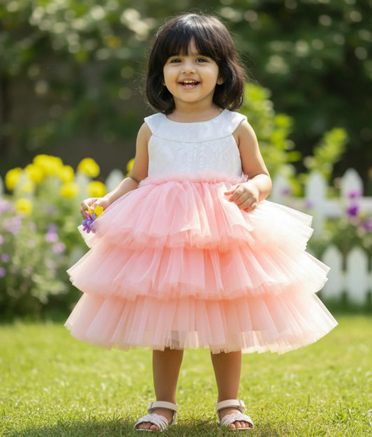 A baby girl wearing a beautiful off-white halter neck and pink tiered tulle net step frock for a birthday celebration.