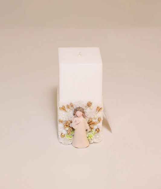 Close-up of a christening candle decorated with an angel charm, gold beads, and white fabric ruffles.