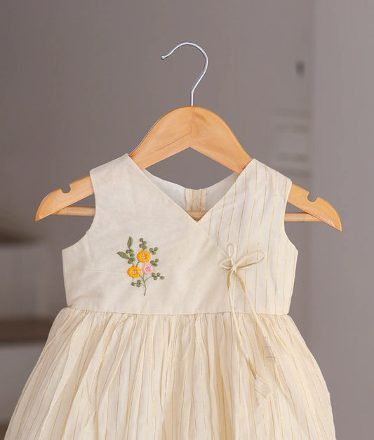 Close-up of the handcrafted pink and yellow flowers and the delicate scalloped hem on the off-white cotton dressv