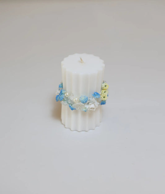 Close-up of a baptism candle featuring light blue and white floral elements with pale yellow accents and pearls