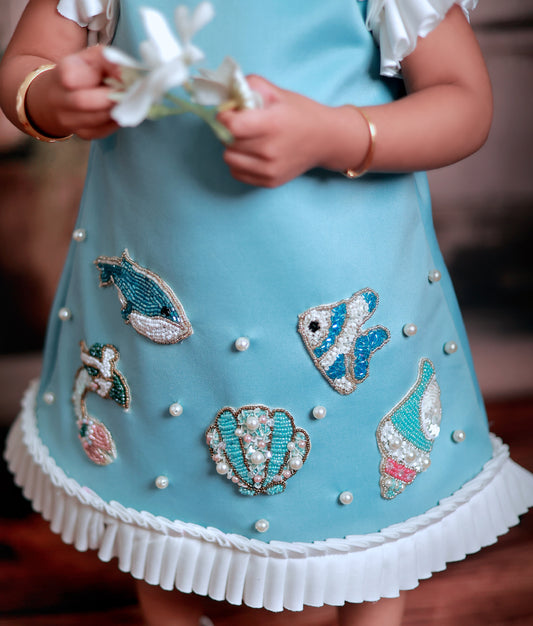 Close-up of the blue mermaid frock showing the hand-worked embroidery on scuba fabric and frilled butterfly sleeves