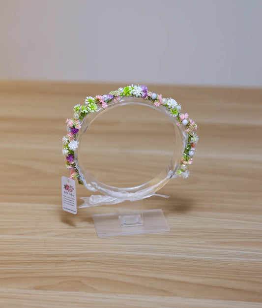 Front view of a handcrafted multi-color floral tiara for baby girls with pastel blossoms and a white ribbon tie
