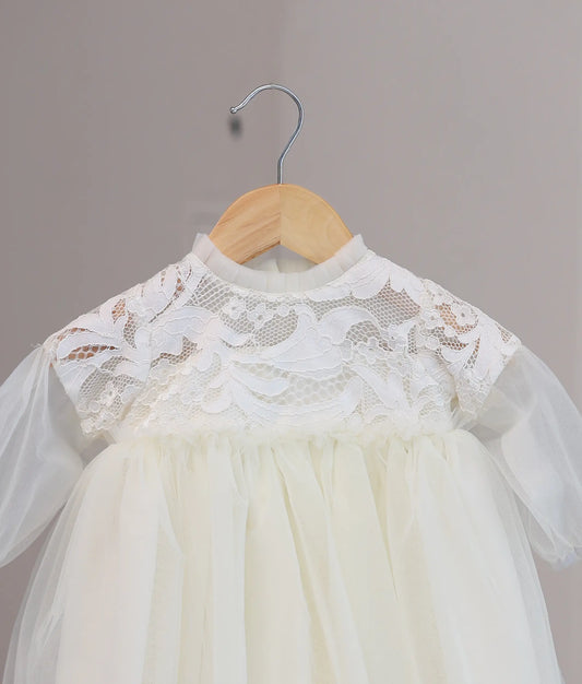 Close-up of the off-white baptism frock showing the textured crochet yoke and the pleated tulle frill at the round neck.