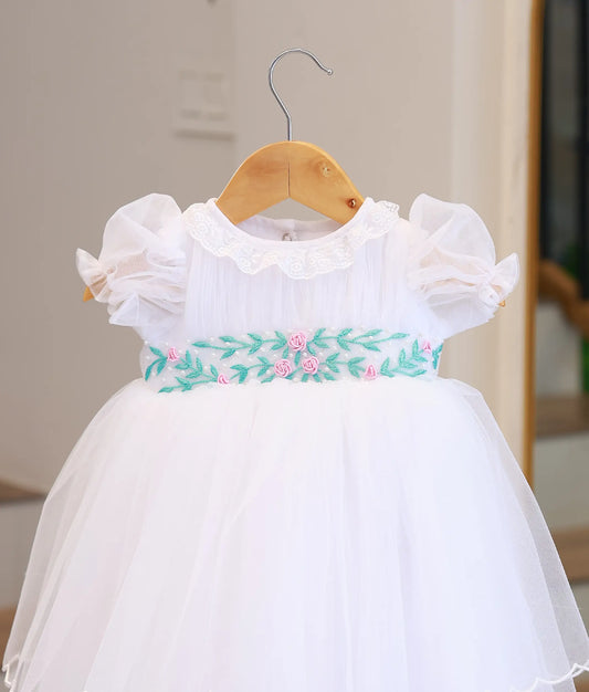 Close-up of the baptism gown showing the intricate pink floral and teal leaf hand-embroidery on the waistband.