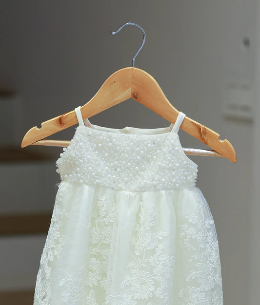 Close-up of the off-white baptism gown showing the intricate yoke adorned with hand-embedded pearls and delicate sequins.
