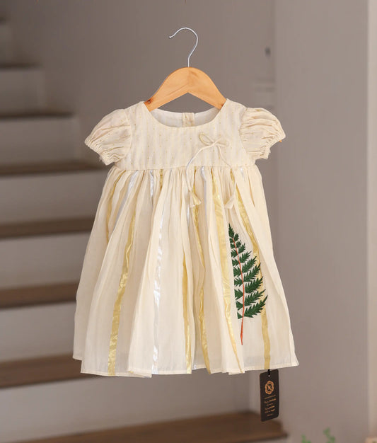 Front view of a traditional off-white cotton baby frock with gold tissue stripes and green leaf embroidery