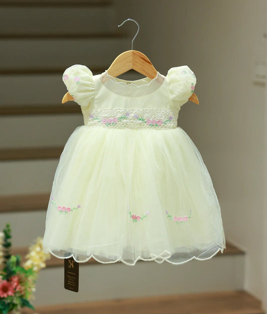 Full front view of an off-white baptism frock featuring a lace-style belt, puffed sleeves, and handworked florals on the skirt hem.