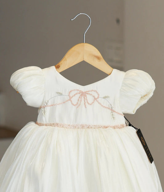 Close-up of the off-white frock highlighting the delicate handworked pink bead bow and floral embroidery on the chest.