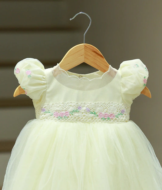 Close-up of the off-white frock showing the frilled round neck, embroidered puffed sleeves, and the lace-like belt on the yoke.
