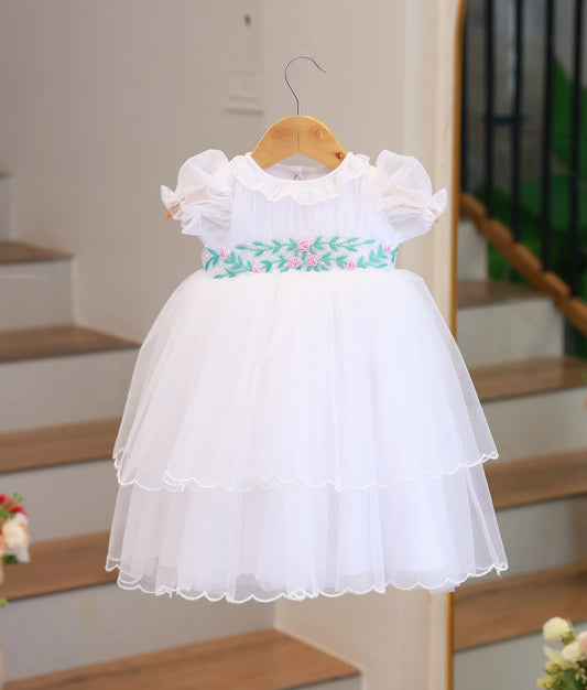 Full front view of an off-white tulle net baptism gown featuring a tiered skirt and hand-embroidered floral waistband.