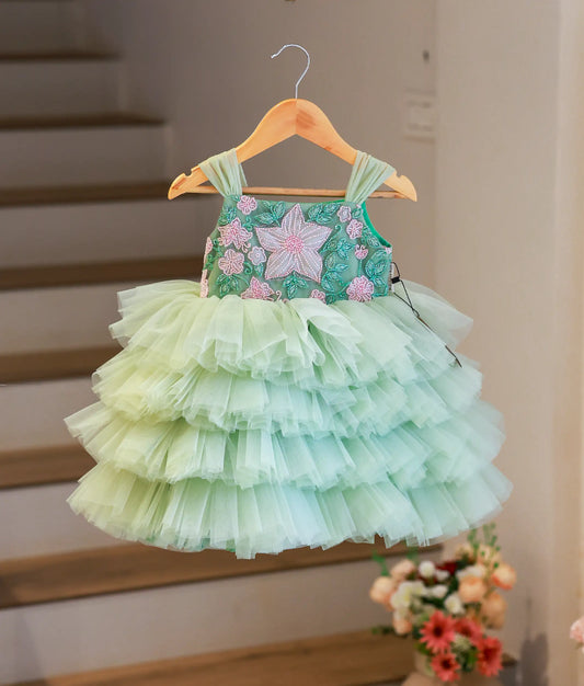 Full front view of a pastel green below-knee party frock for girls featuring a tiered tulle skirt and floral handworked bodice.