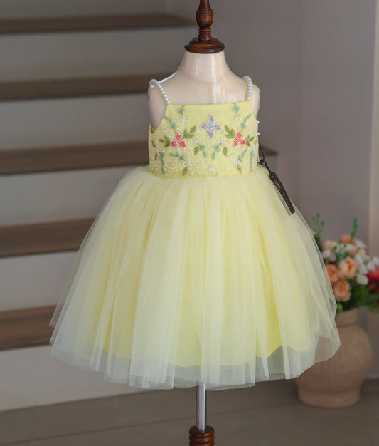 Front view of a pastel yellow tulle frock with floral handwork and thin pearl straps.