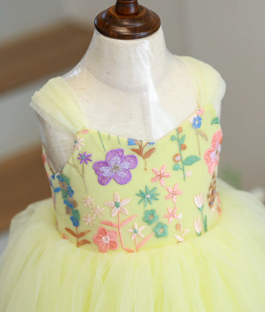 Close-up of the pastel yellow gown showing the intricate multi-colored floral embroidery on the work material yoke and tulle shoulder accents.