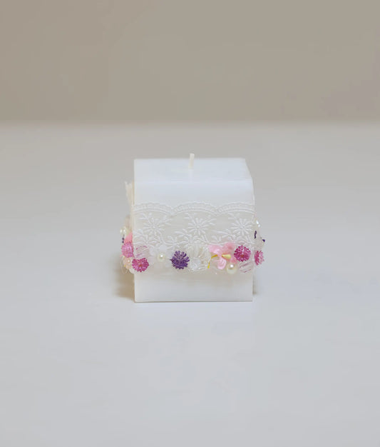 Decorative baptism candle featuring pink and purple silk flowers, white lace ruffles, and pearl accents