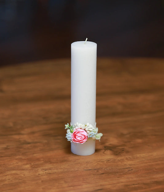 Front view of a white baptism candle decorated with pink and white flowers and a pink satin ribbon