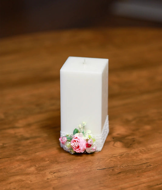 Front view of a white baptism candle decorated with pink and white flowers and a layered satin ribbon