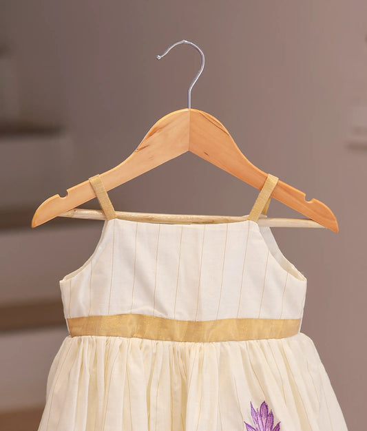 Close-up of the purple floral embroidery and the gold-lined fabric on the off-white kasavu frock.