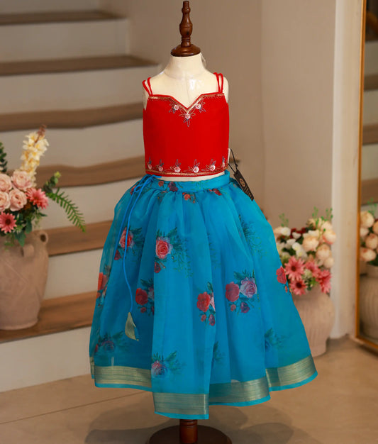 Full-length view of a girl's ethnic set featuring a red sleeveless handworked top and a layered blue floral organza skirt with a gold border