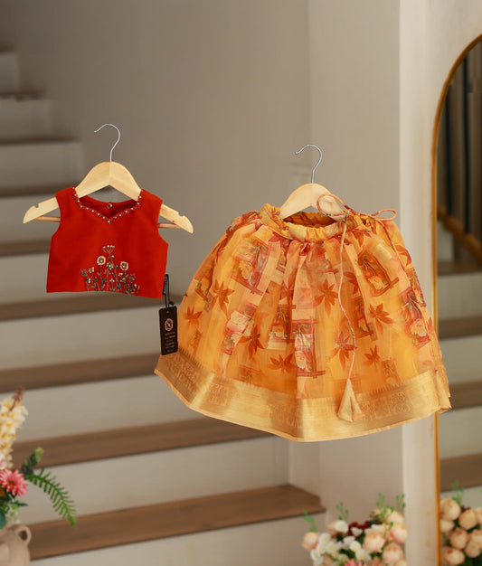 A girls' ethnic set featuring a sleeveless red handworked short top and a yellow floral print organza skirt with a gold border
