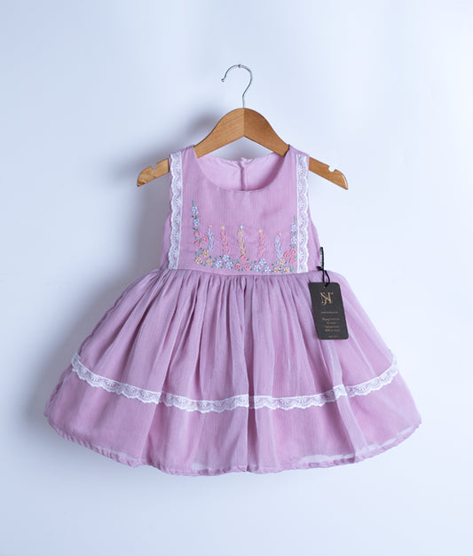 A baby pink sleeveless frock hanging on a hanger against a white background.