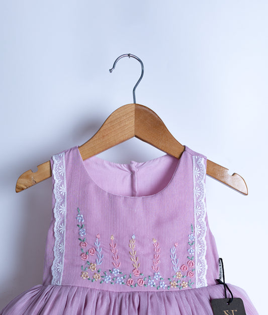 Close view of an baby pink sleeveless frock hanging on a hanger against a white background.
