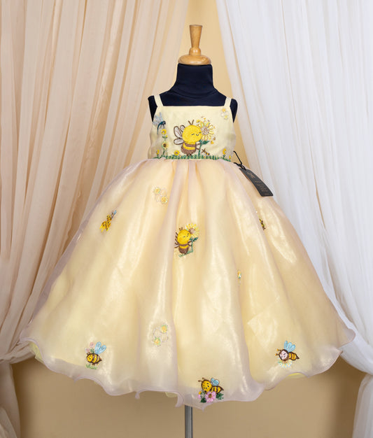 Golden dress with honeybee theme on a mannequin against a beige curtain background.