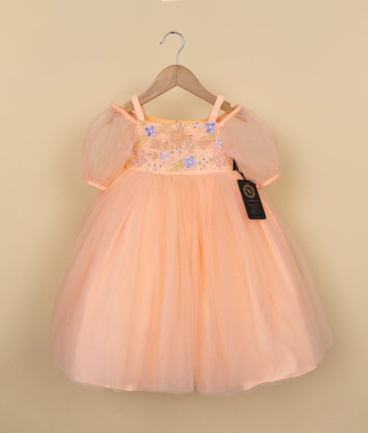 Peach-colored dress with floral embellishments on a hanger against a beige background.