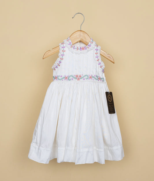 Sleeveless white baby dress with pastel floral embroidery on neck and waist, displayed on wooden hanger against beige background