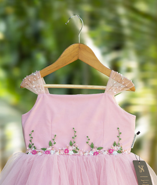 Pink baby girl frock with floral embroidery, beaded waist design, and sheer polka dot shoulder straps – elegant party dress displayed on wooden hanger.