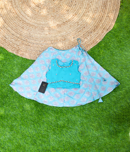 Sky blue handwork top with peach skirt laid out on a green surface, traditional wear.