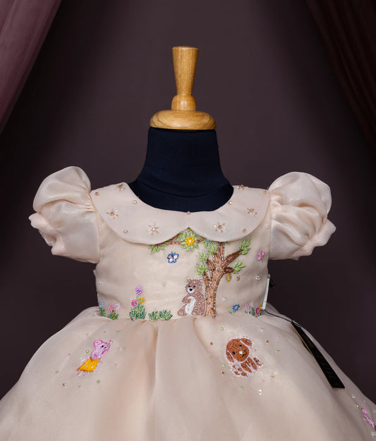 Close view of a beige baby girl dress with puff sleeves, a Peter Pan collar, and cartoon forest animal embroidery.