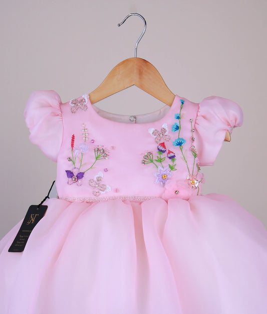 Close view of a plain pink organza baby girl frock with embroidered butterfly and floral designs on the bodice