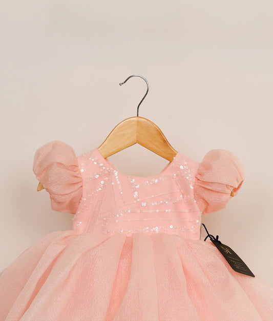 Close view of a pastel pink crush organza birthday frock against plain background