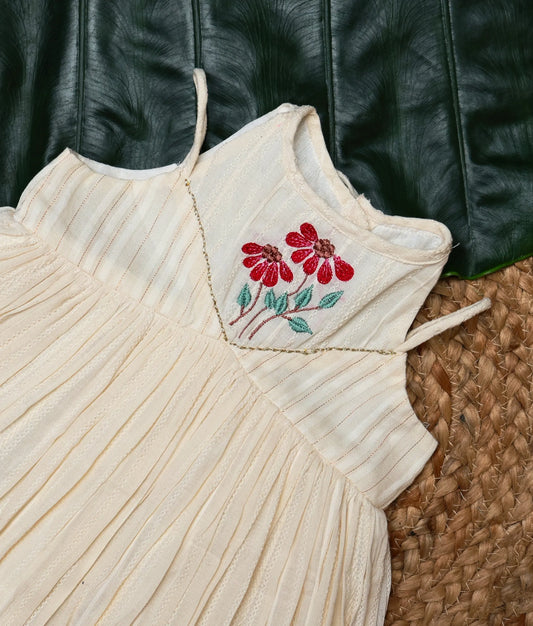 Close view of a traditional off-white baby girl dress with red floral embroidery and a red border, festive ethnic wear.