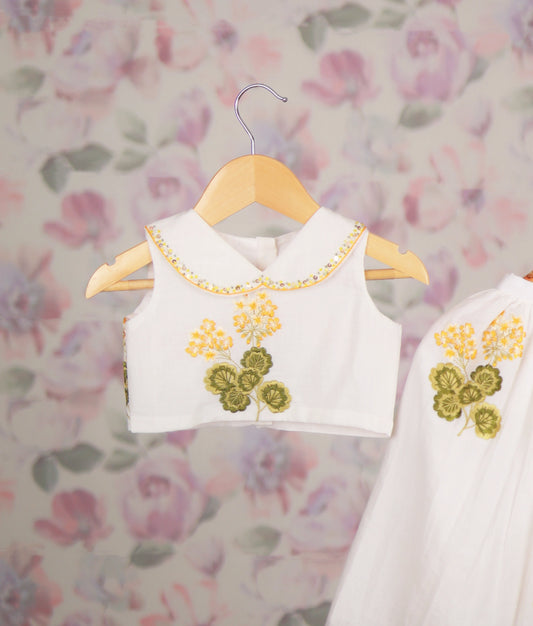 Close view of a white baby girl skirt set with yellow floral embroidery and a Peter Pan collar top, ethnic wear.