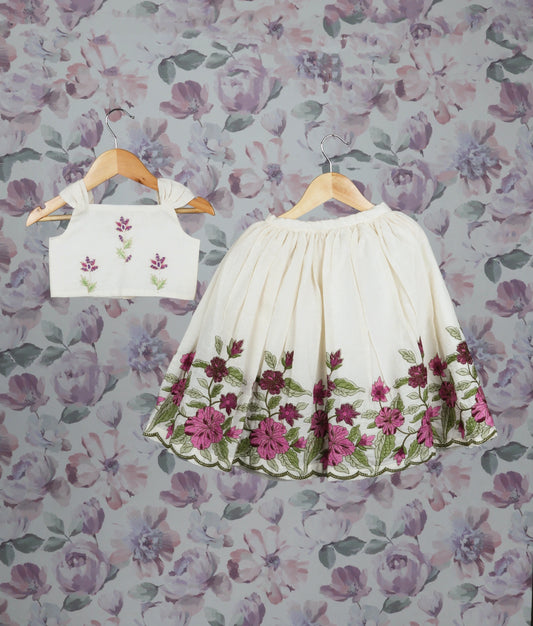 Floral embroidery top and skirt set on hangers against a floral wallpaper background.
