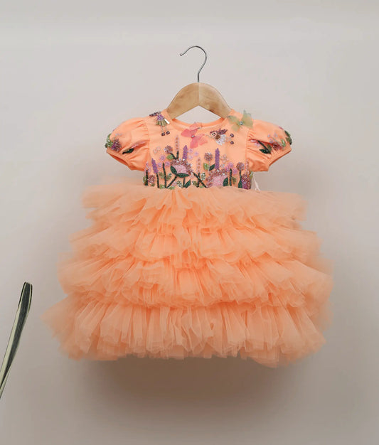 Front view of peach handworked and embroidery floral design butterfly-themed birthday frock against plain background