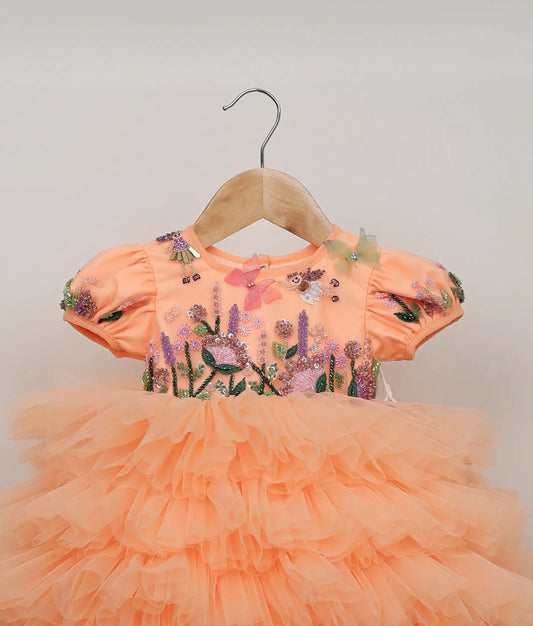 Close view of peach handworked and embroidery floral design butterfly-themed birthday frock against plain background
