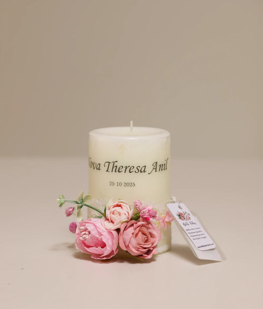 Front view of an off-white small pillar candle with a customized baptism name and date, featuring pink floral accents and lace. A beautiful keepsake.