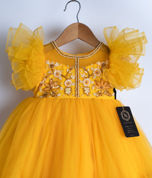 Close view of an yellow tulle net frock displayed on a hanger.