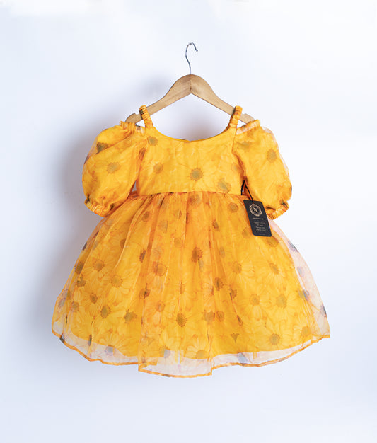 A yellow printed organza frock with puffed sleeves, displayed on a hanger against a white background.